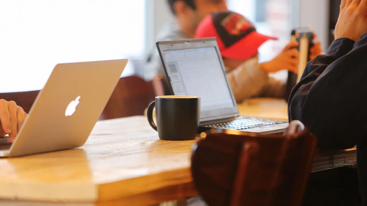 Travailler dans des cafés en tant que freelance freelances lyonnais travaillant dans un café confortable avec des ordinateurs portables et des mugs à café sur une table partagée.